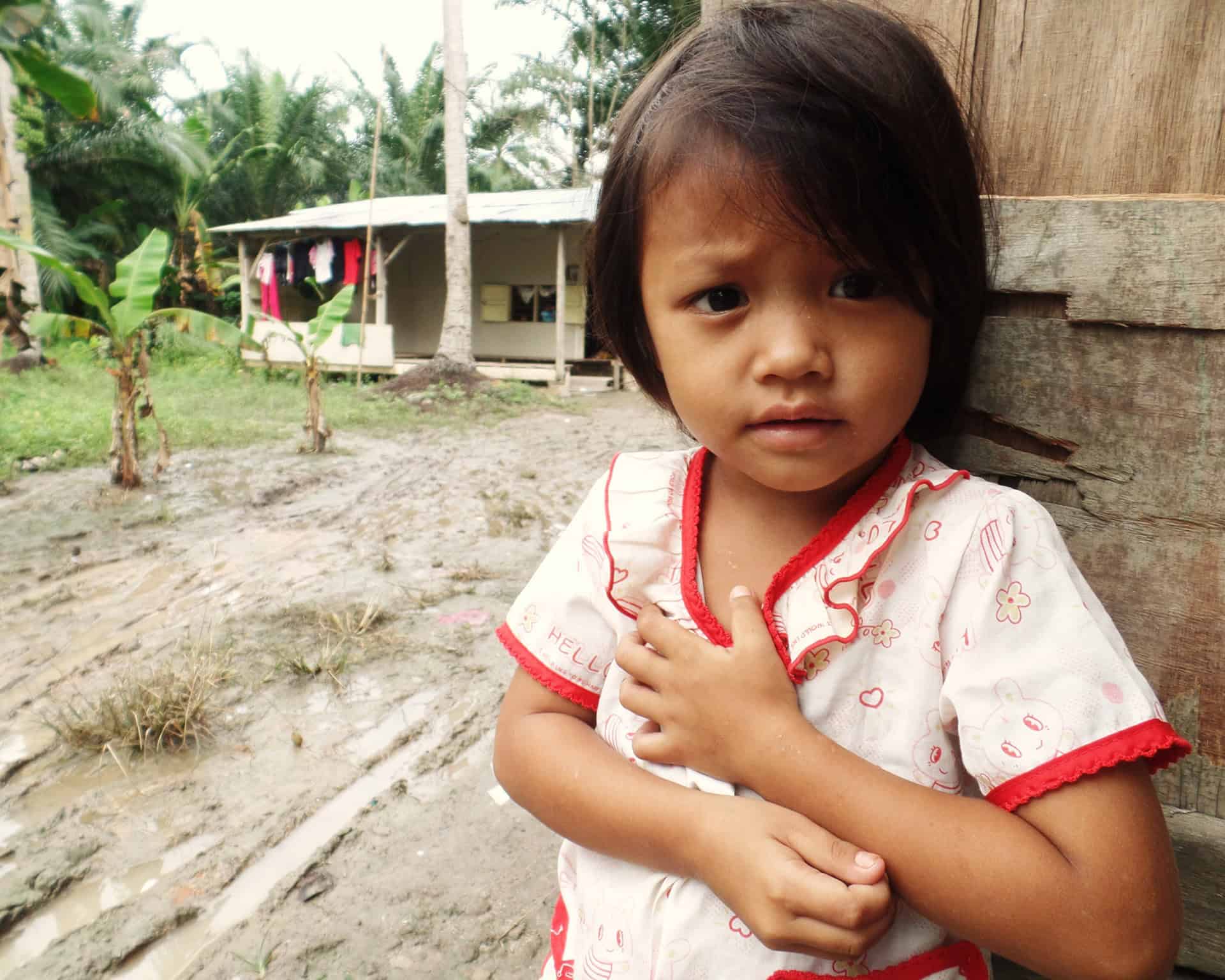 An orang Asli child stands outside her wooden house.