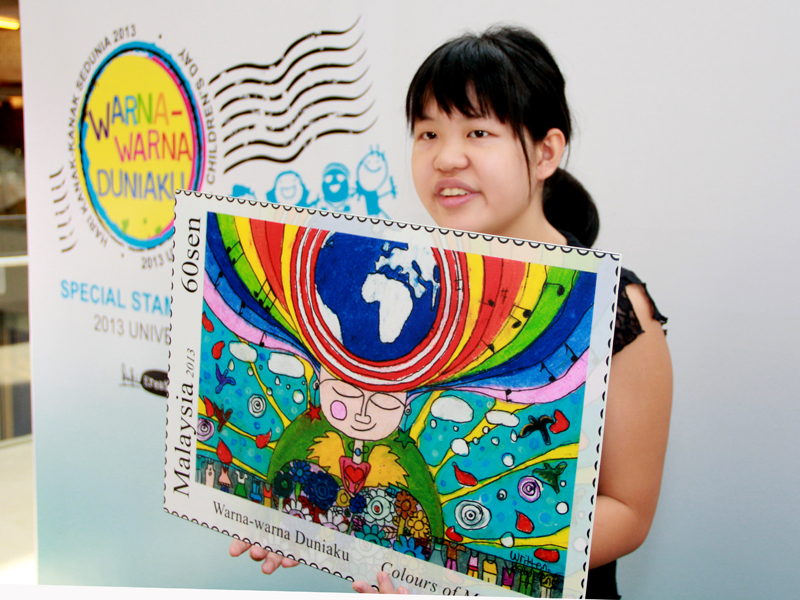 A girl holds up a mock up of a stamp for the Colours of My World drawing competition.