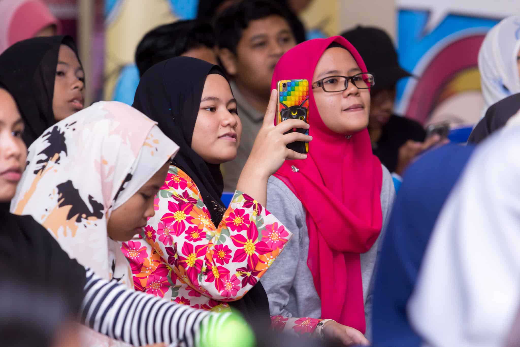 a group of girls. One girl is holding up her phone to take a photo.