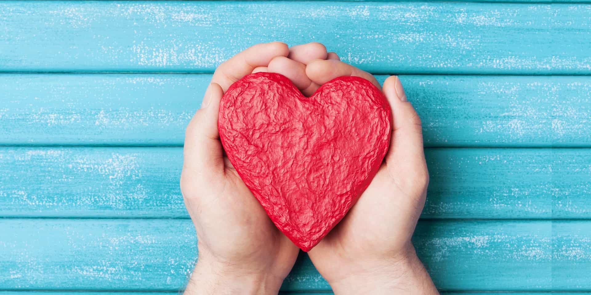 An paper mache designed in the shape of a heart is cradled in the palms of two hands..