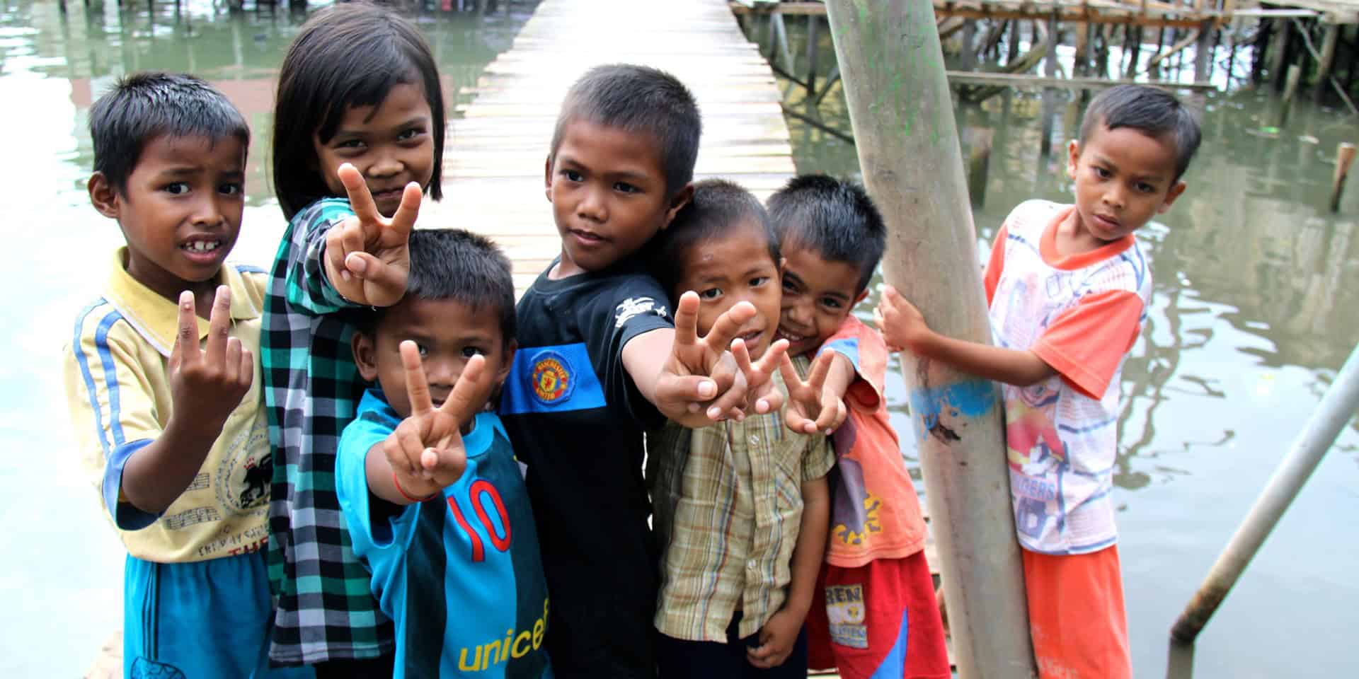 a group of children from a water village holding up the peace sign with their fingers.