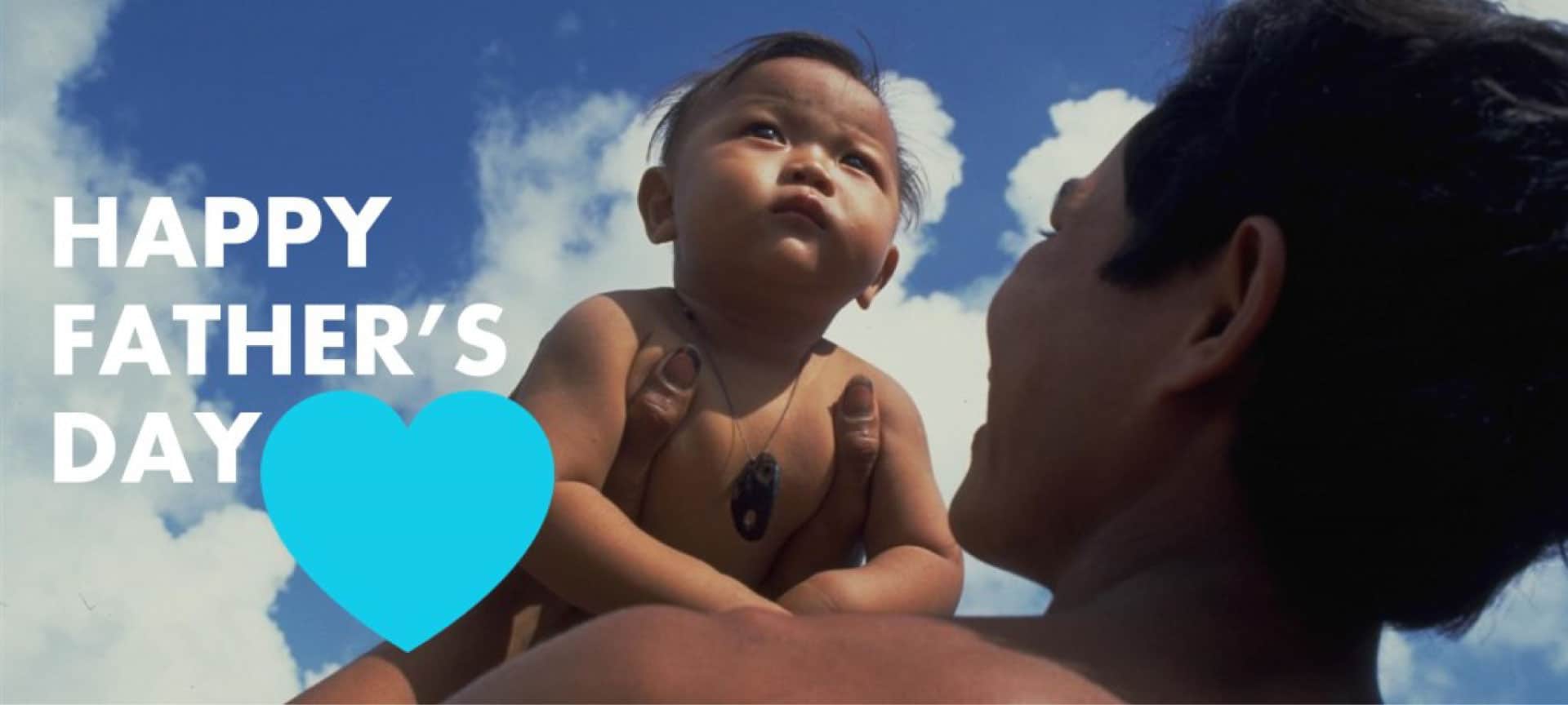 A father holds up his infant son. Next to him are the words Happy Father's Day.