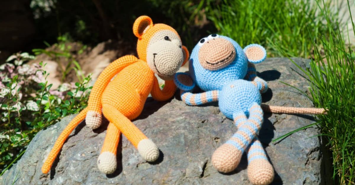 Two stuffed toy monkeys, one orange, one blue, basking under the sun in the garden.