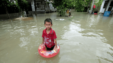 a boy stands in flood waters in front of his home in Malaysia.