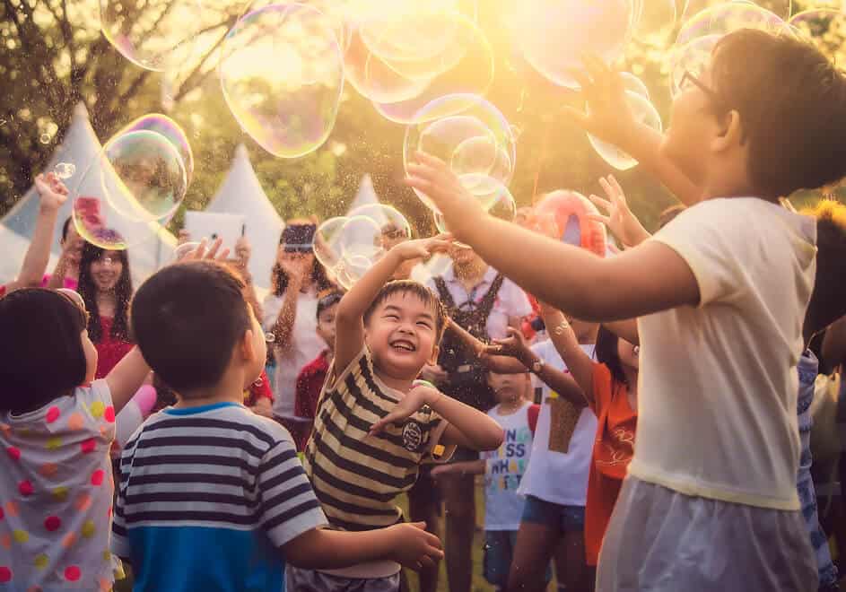 A GROUP OF YOUNG CHILDREN PLAYING WITH BUBBLES TOGETHER WHILE SMILING