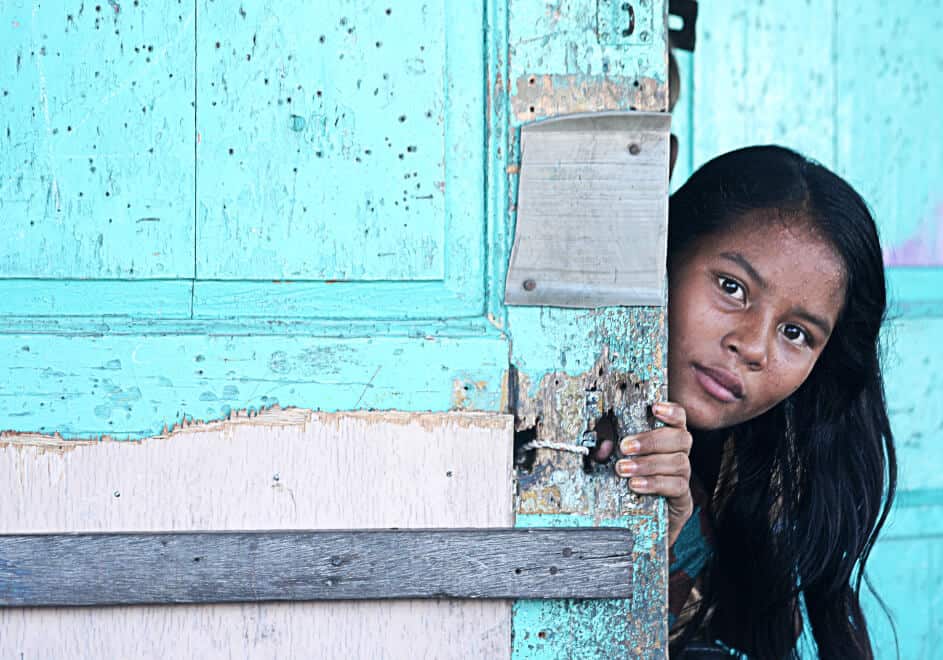 A YOUNG ADOLESCENT GIRL STANDING BEHIND A WALL LOOKING AT THE CAMERA