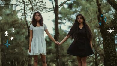 Two friends hold hands while walking through trees.