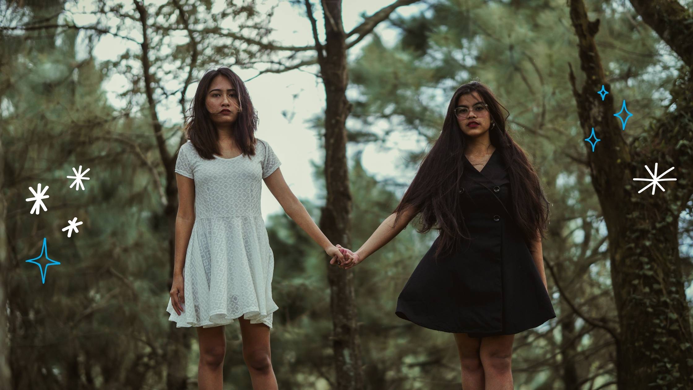 Two friends hold hands while walking through trees.