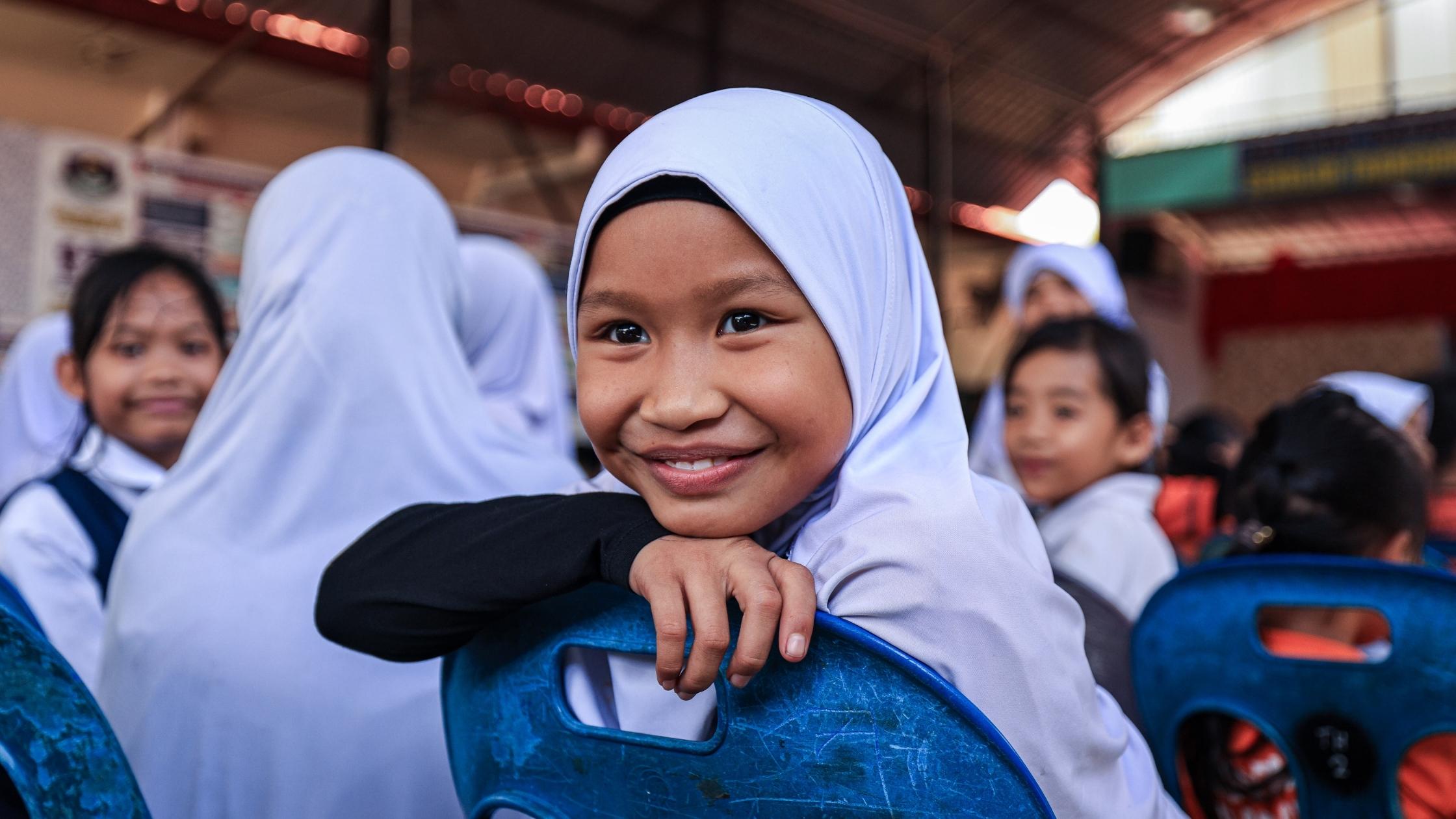 A smiling girl sitting in her classroom.