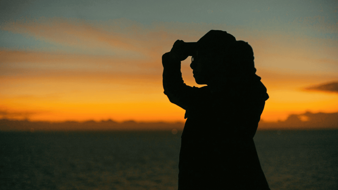 A teenage girl looks out to the sunset at the beach.