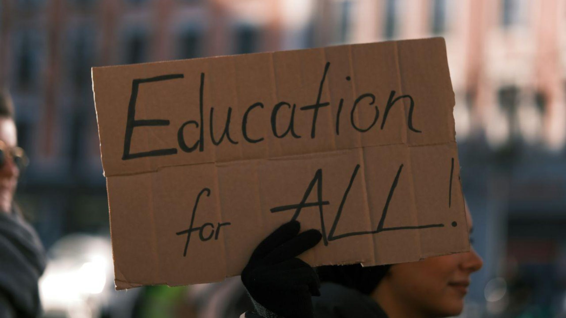 A hand holds up a placard that says "Education for All".