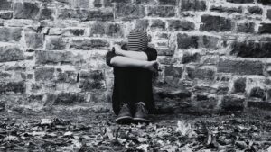 Young man sitting on the ground against a brick wall.