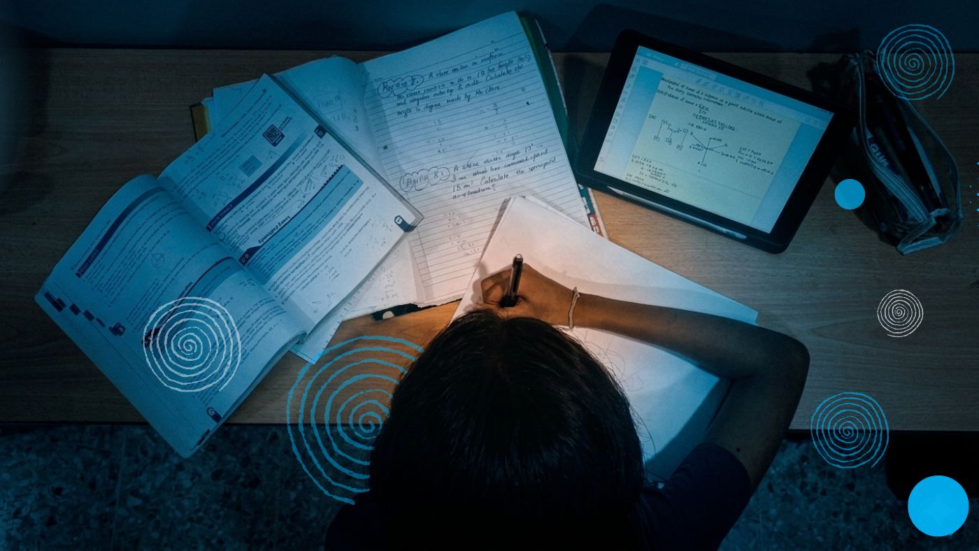 A young girl studying at her desk with school books around her.
