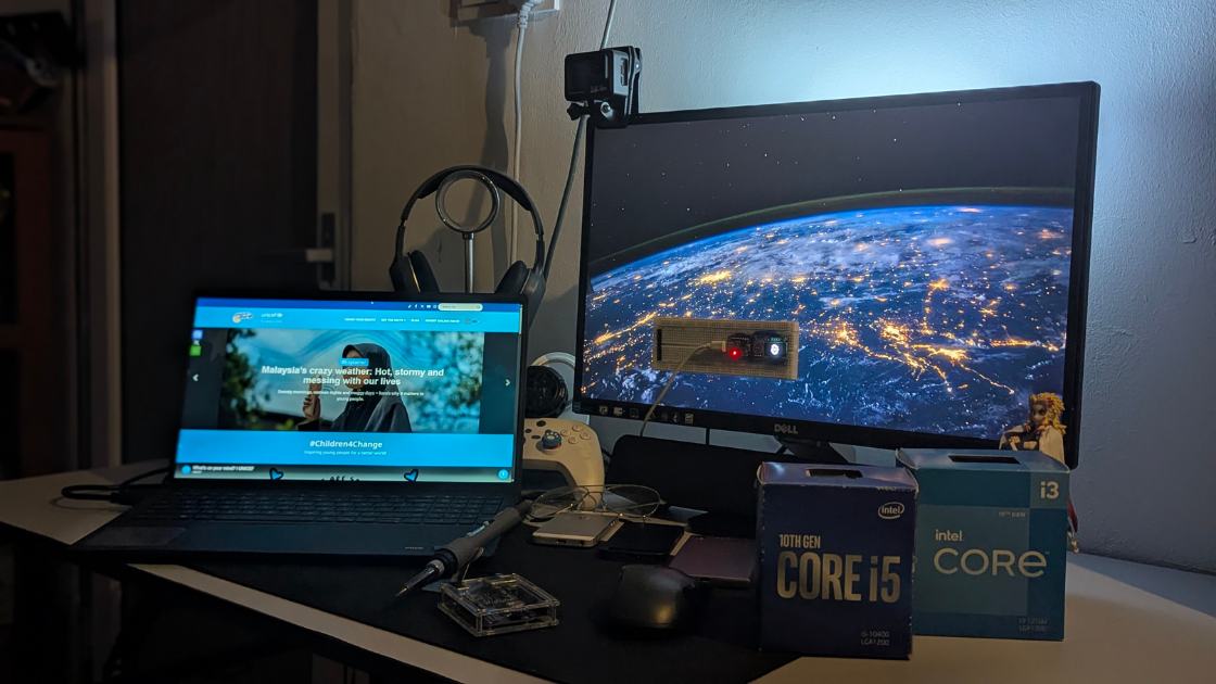 A desk with a laptop, monitor and DIY electronics setup, including a breadboard with LED lights and tools.