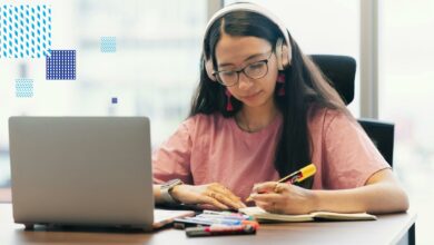 A university student using a laptop while taking notes and highlighting study materials at a desk.