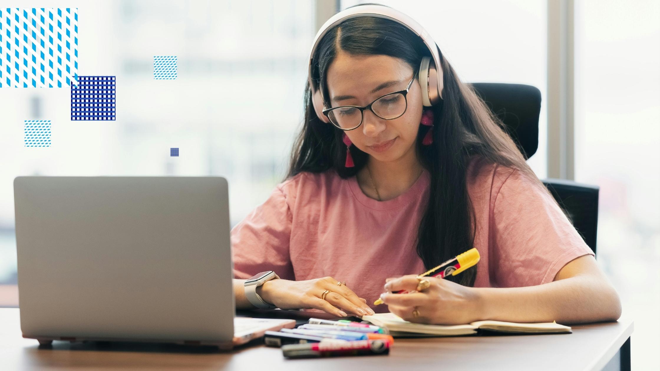 A university student using a laptop while taking notes and highlighting study materials at a desk.